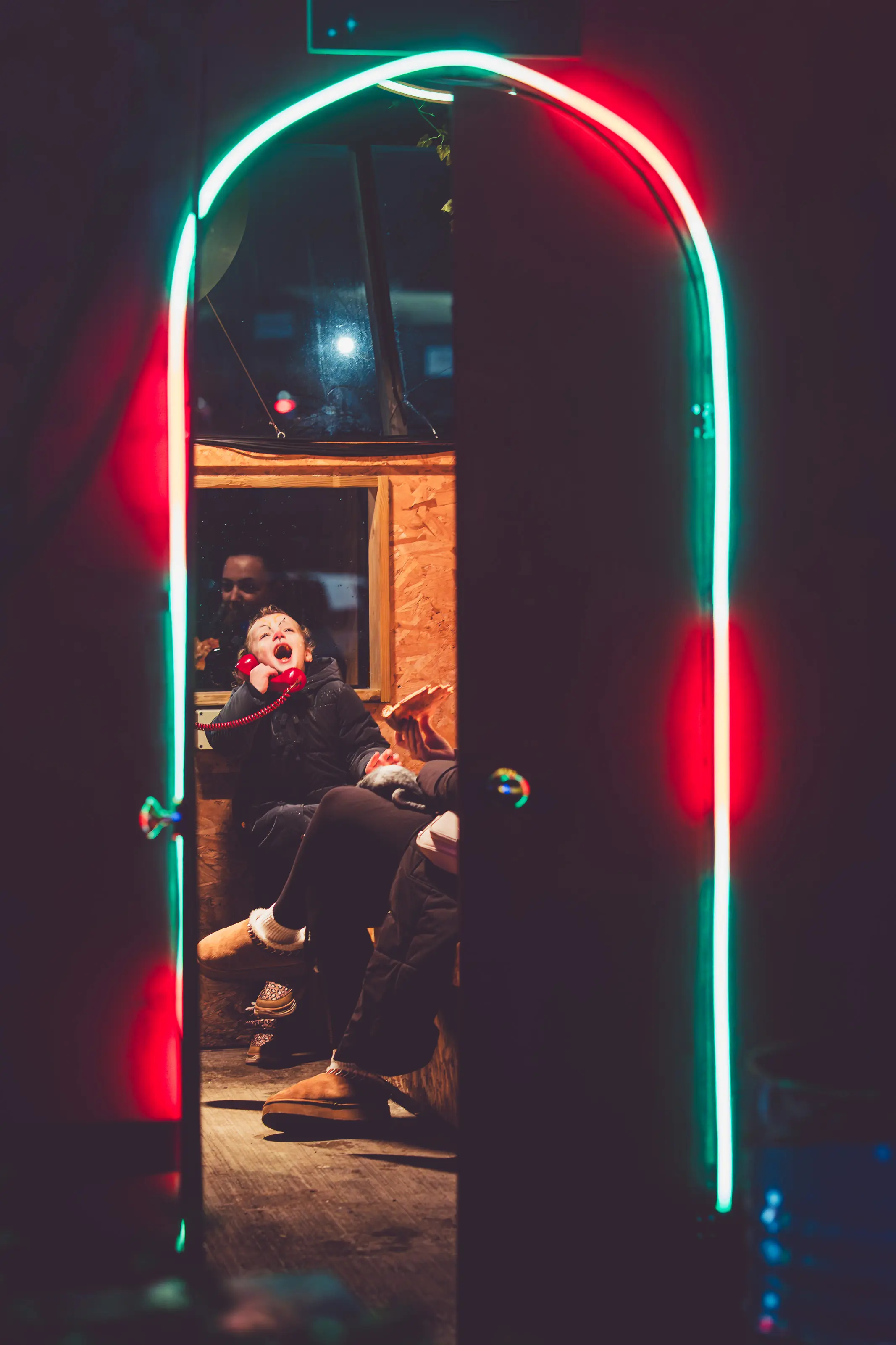Portrait of a Twilight Tales visitor listening closely on a landline handset under magenta lighting